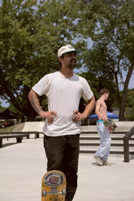 An image of five young adults standing on a lawn surrounded by trees holding flowers.